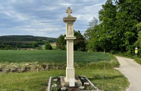 Urlauberkreuz Bösendürnbach, © Weinstraße Weinviertel Steinkreuz auf einem Feldweg mit grüner Landschaft im Hintergrund.