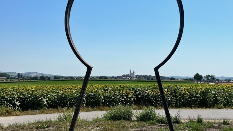 Blick auf Wullersdorf, © Weinstraße Weinviertel Metallrahmen in Form eines Schlüssellochs mit Blick auf Wullersdorf und Sonnenblumenfeld.