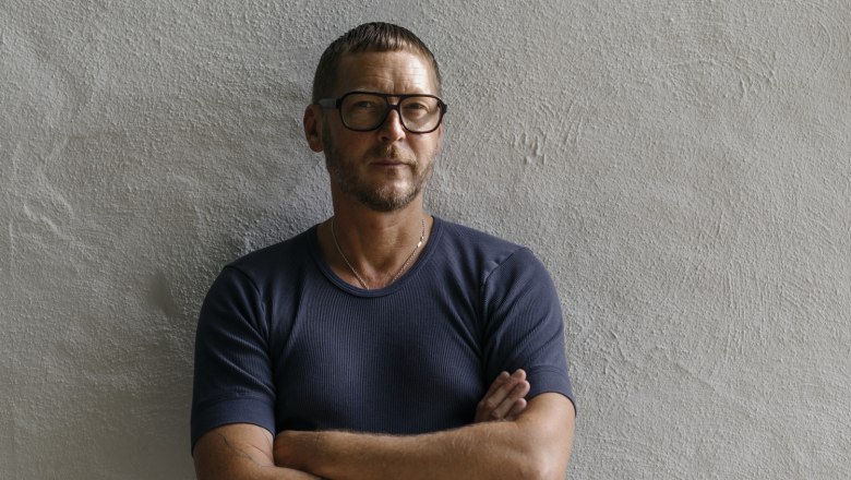 Harald Pollak interpretiert Wirtshausklassiker neu, © Niederösterreich Werbung/Julius Hirtzberger Mann mit Brille und tätowierten Armen steht vor einer weißen Wand.