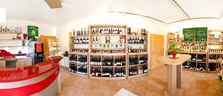 Wein & Genuss, © Elisabeth Hausgnost Innenansicht eines Weinladens mit Regalen voller Weinflaschen und einem roten Tresen.