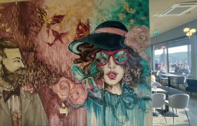 Rooftop Eingangsbereich, © Rebecca Freitag Wandgemälde mit stilisierten Porträts eines Mannes und einer Frau in einem Café.