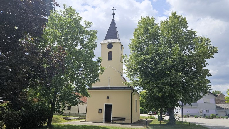 Barbara Kapelle Kleinweikersdorf, © Barbara Sturmlechner Die Barbara Kapelle in Kleinweikersdorf, umgeben von Bäumen und einem gepflegten Rasen, bei sonnigem Wetter.