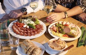 Heuriger Humer, © Humer Zwei Personen sitzen an einem Tisch mit Wurst- und Käseplatten, Brot und Wein.