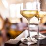 Den Wein genießen, © Weinviertel Tourismus GmbH / Herbst Zwei Weingläser mit Weißwein auf einem Tisch, unscharfer Hintergrund.
