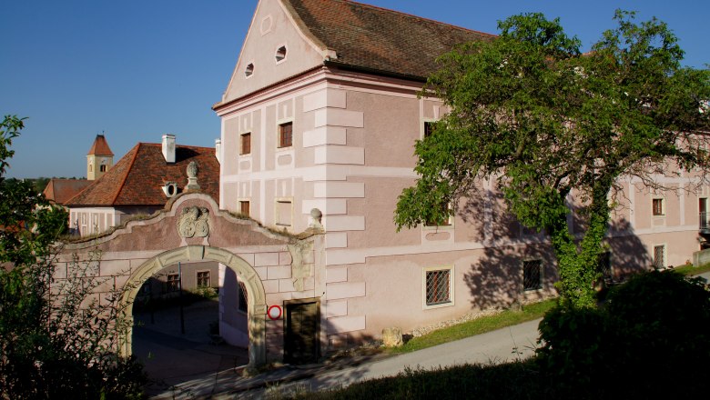 Europahaus Pulkau, © Fotoclub Pulkau Historisches Gebäude mit rosa Fassade und Torbogen, umgeben von Bäumen.