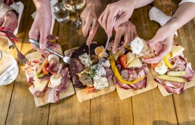 Heurigenjause, © Weinviertel Tourismus GmbH / Herbst Mehrere Hände greifen nach Wurst- und Käseplatten auf einem Holztisch.