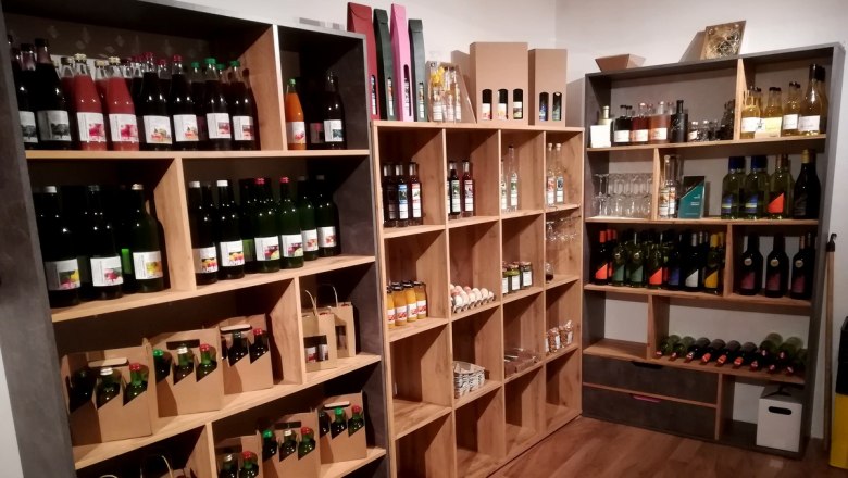 Reichhaltiges Angebot im Hofstüberl, © Erlebnishof Huber Regale mit verschiedenen Flaschen und Produkten in einem Hofladen.