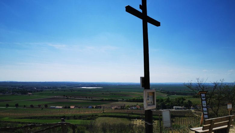 Freiheitskreuz mit wunderbarem Fernblick, © Weinstraße Weinviertel Ein großes Holzkreuz auf einem Hügel mit Blick auf eine weite Landschaft unter blauem Himmel.