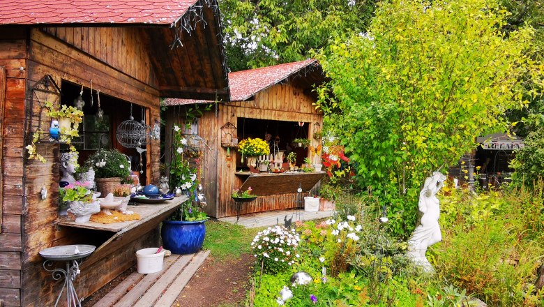 Keramik Slama, © Weinstraße Weinviertel Garten mit Holzhütten, Pflanzen und Keramikdekorationen.