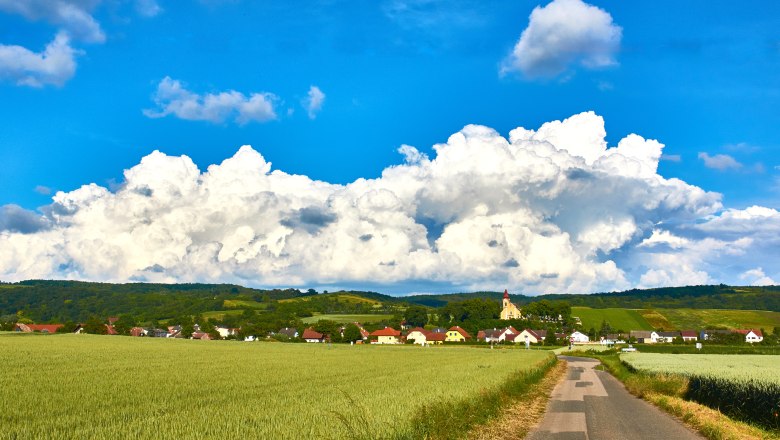 Frauendorf, © M. Greil Landschaft mit Dorf, Feldern und Kirche vor großen Wolken.