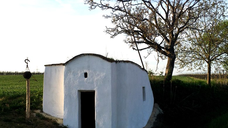 Hiatahütte Großmeiseldorf, © Marktgemeinde Ziersdorf Weiße Hiatahütte auf einem Feld mit Bäumen und einem Holzpfosten daneben.