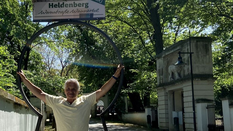 Heldenberg beim Schloss, © Weinstraße Weinviertel Ein Mann steht in einem großen, schlüsselförmigen Rahmen mit einem Schild "Heldenberg Weinstraße Weinviertel" darüber.