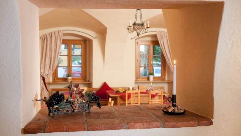 Zirbenstüberl, © Althof Retz Blick durch eine Maueröffnung in einen gemütlichen Raum mit Holzmöbeln und Kerzenlicht.