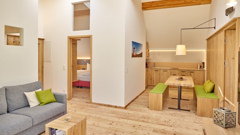 Weinviertler Kellerstöckl, © Weingut Hindler Modernes Wohnzimmer mit Holzmöbeln, grauem Sofa und offener Küche.