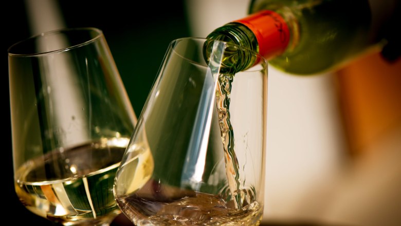 Landhaus Krell, © Weingut Krell Weißwein wird in ein Glas eingeschenkt, daneben ein weiteres gefülltes Glas.