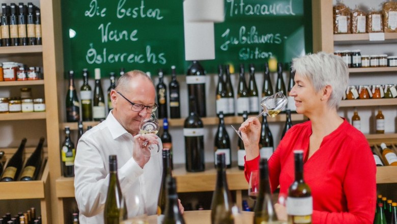 Wein & Genuss, © Elisabeth Hausgnost Zwei Personen verkosten Wein in einem Geschäft mit Weinflaschen im Hintergrund.