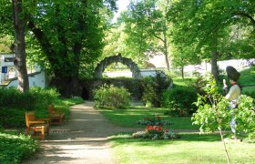 Englischer Garten, © Josef Stefan Ein grüner Garten mit Bäumen, Bänken und einer Statue.