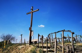 Freiheitskreuz in Haugsdorf, © Weinstraße Weinviertel Holzkreuz auf einem Hügel mit Weinreben und blauem Himmel im Hintergrund.