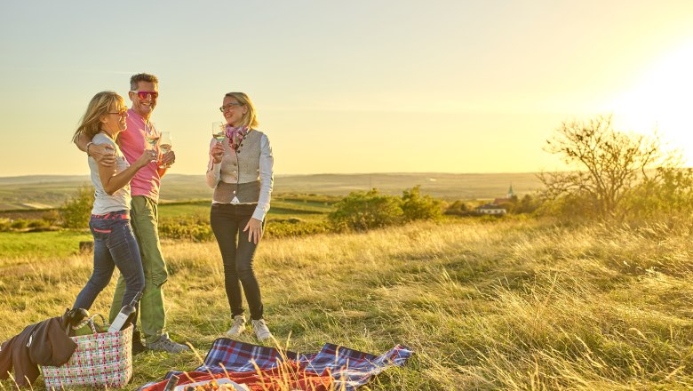 Picknicken in Schrattenthal, © Weingut Hindler Drei Personen beim Picknick auf einer Wiese bei Sonnenuntergang.