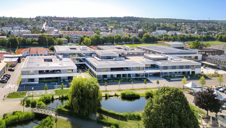 Schulcampus und Stadt Hollabrunn, © Romana Fürnkranz Luftaufnahme eines modernen Schulcampus mit Solarpanelen auf den Dächern, umgeben von Grünflächen und einem Teich im Vordergrund.
