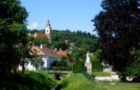 Pfarrkirche Zemling, © Marktgemeinde Hohenwarth-Mühlbach Landschaft mit Kirche und Statue in einem Dorf.
