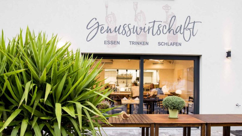 Schönes Ambiente drinnen und draußen, © Genusswirtschaft Außenansicht eines Restaurants mit der Aufschrift 'Genusswirtschaft'.