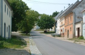 Straße mit traditionellen Gebäuden und Bäumen in einer ländlichen Umgebung.