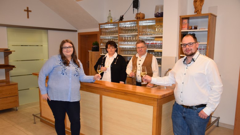 Vier Personen stehen an einer Theke und halten Weingl&auml;ser in der Hand.