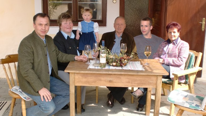 Eine Familie sitzt an einem Holztisch im Freien, mit Wein und Dekoration auf dem Tisch.
