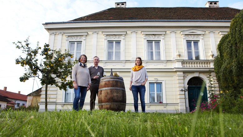 Drei Personen stehen vor einem historischen Gebäude mit einem Weinfass im Vordergrund.