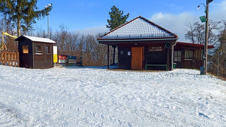 Schneebedeckte Schiclub-Hütte mit Holzhäuschen und Bäumen im Hintergrund.