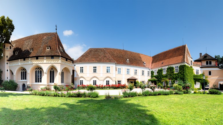Panoramablick auf das Schloss Schrattenthal mit gepflegtem Garten und blühenden Rosen im Vordergrund.