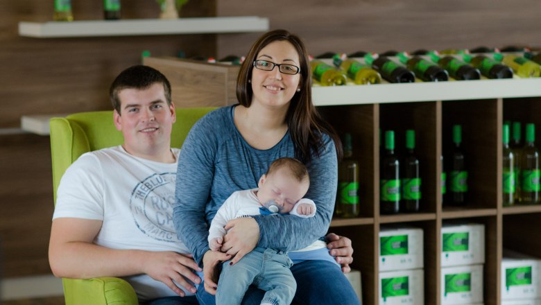 Ein Paar mit einem Baby sitzt auf einem grünen Sessel in einem Weingut.