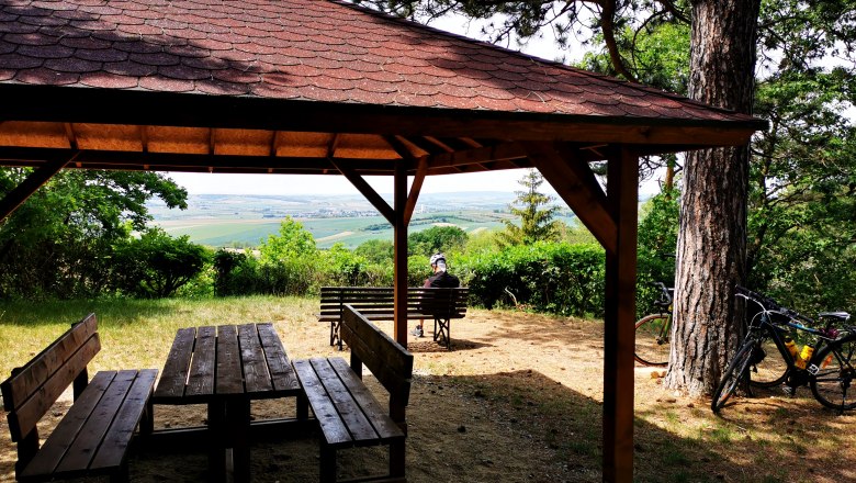 Holzpavillon mit Tisch und Bänken, Blick auf Weinberge, Fahrrad an einem Baum.