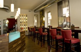 Innenansicht eines modernen Restaurants mit roten Stühlen und hölzernem Tresen.