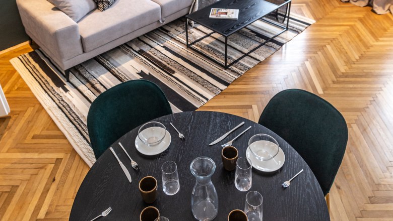 Modernes Wohnzimmer mit Sofa, Couchtisch, Teppich und Esstisch mit Gedeck.