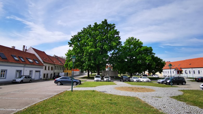 Hauptplatz in Sitzendorf an der Weinstraße mit parkenden Autos und Bäumen.