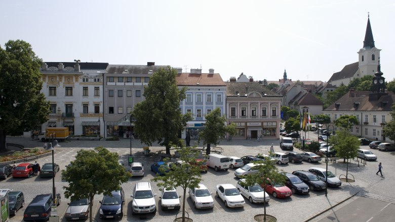 Stadtplatz in Hollabrunn mit geparkten Autos, historischen Gebäuden und einer Kirche im Hintergrund.