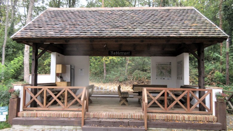 &Uuml;berdachte Raststation f&uuml;r Radfahrer im Wald mit Sitzgelegenheiten und Informationsschildern.