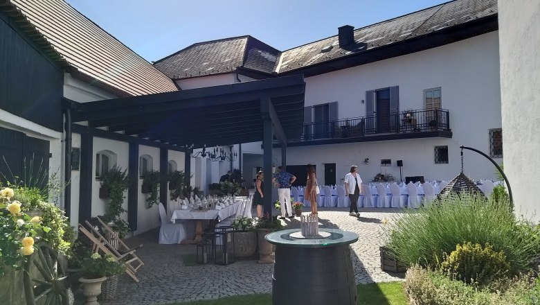 Innenhof mit gedeckten Tischen, Blumen und Personen bei sonnigem Wetter.