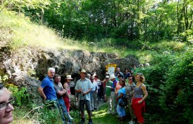 Gruppe von Menschen vor einer H&ouml;hle im Gr&uuml;nen.