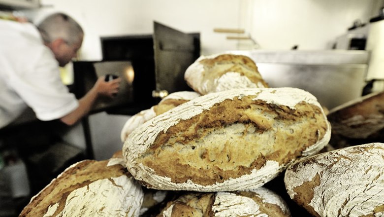 Frisch gebackenes Brot vor einem Bäcker, der einen Ofen bedient.