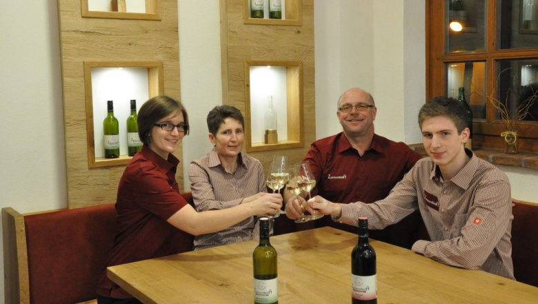 Vier Personen stoßen mit Weingläsern an einem Tisch an.