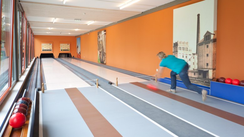 Person beim Kegeln auf einer Kegelbahn mit orangefarbener Wand.