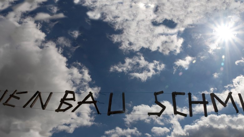 Holzschriftzug 'Weinbau Schmid' vor bewölktem Himmel und Sonne.