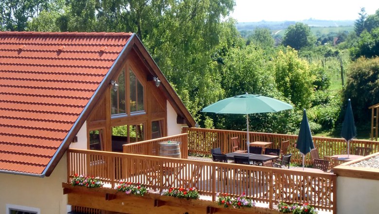 Terrasse mit Holzzaun, Tischen und Sonnenschirmen, umgeben von grüner Landschaft.