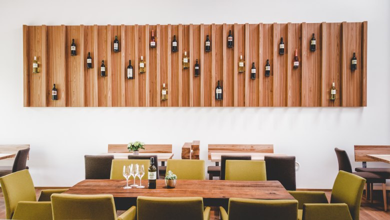 Innenansicht eines modernen Heurigen mit Holztischen und Weinflaschen an der Wand.