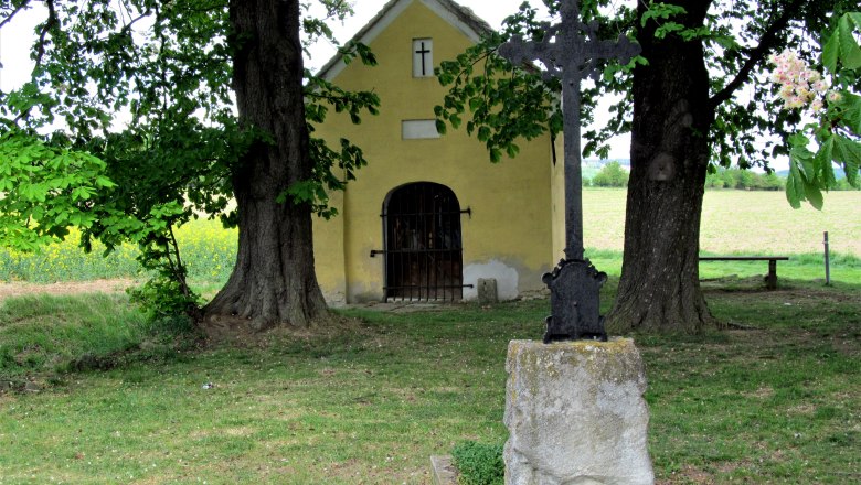 Gelbe Kapelle mit Kreuz und Bäumen im Vordergrund.