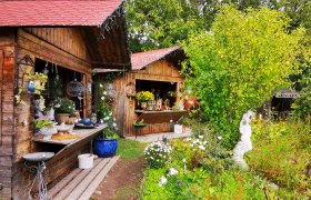 Garten mit Holzhütten, Pflanzen und Keramikdekorationen.