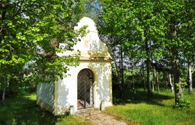 Kleine Kapelle umgeben von Bäumen im Grünen.